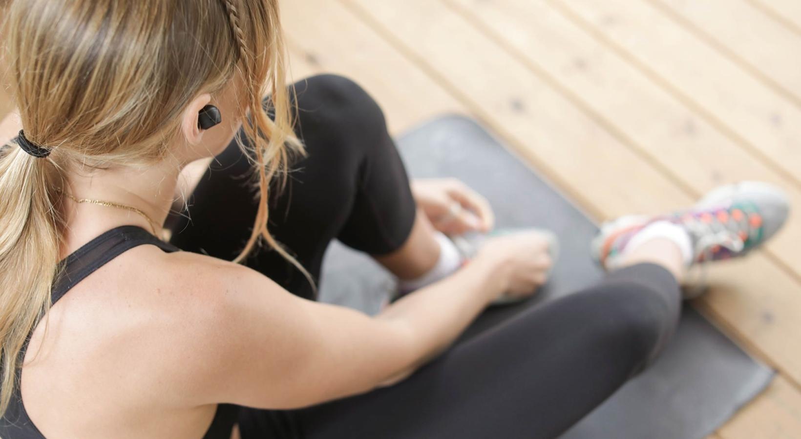 Get your workout on woman in workout gear, sits on a yoga mat and ties her shoe