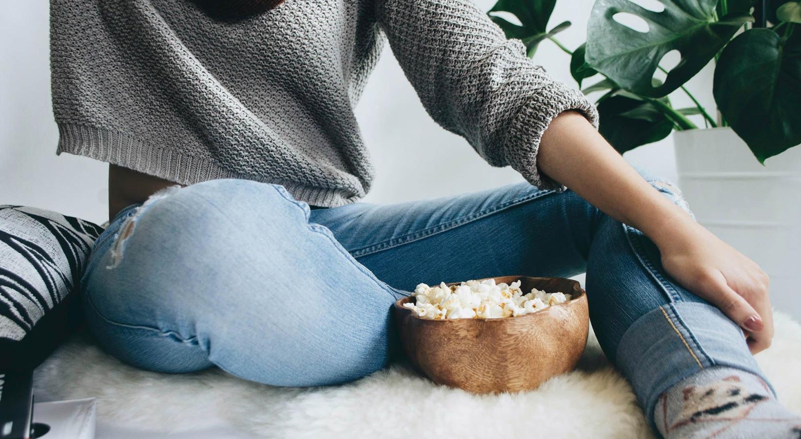 All the comforts of luxury living woman sits on a rug with a bowl of popcorn