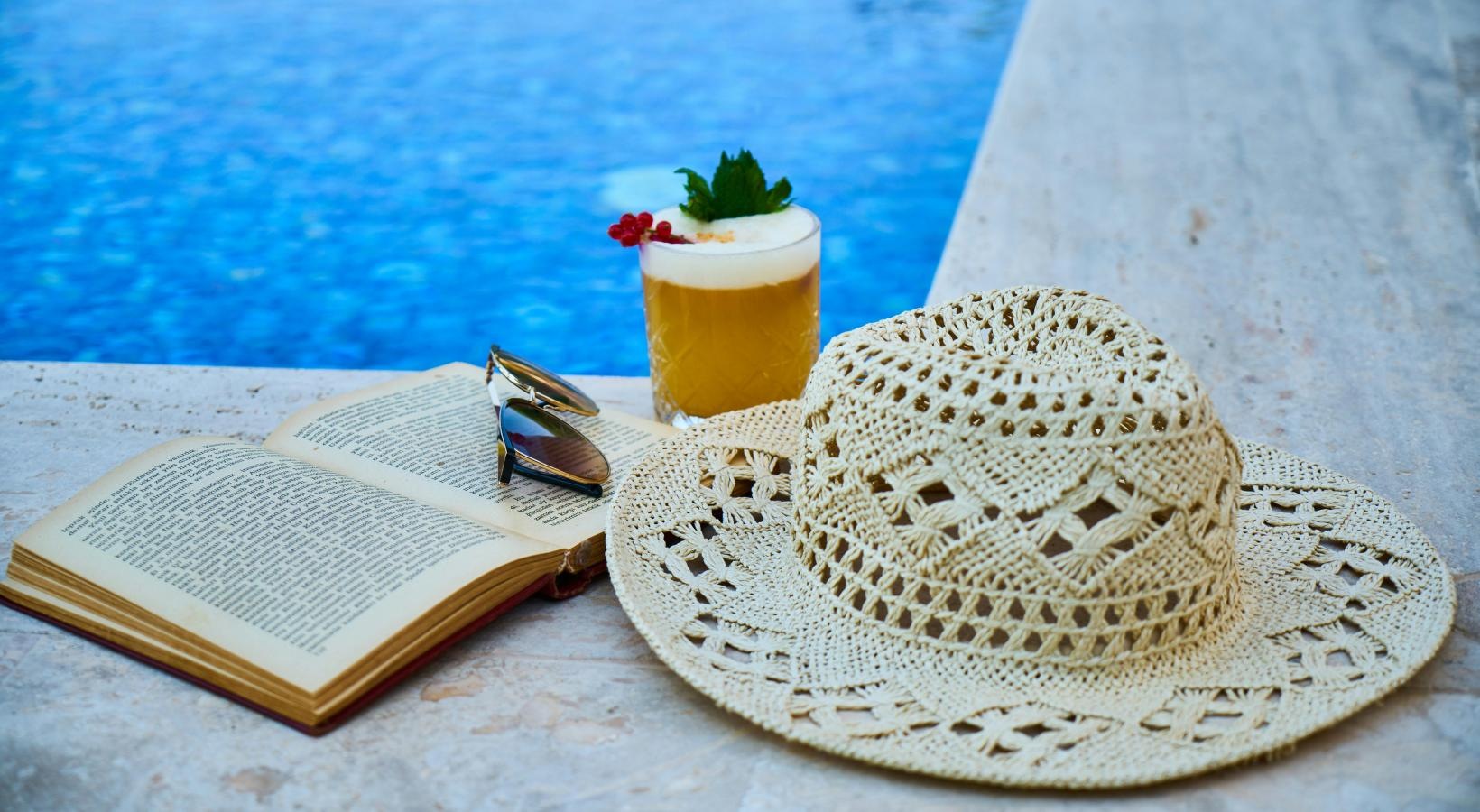Shimmering resort-style pool a hat and a book on a table by a pool