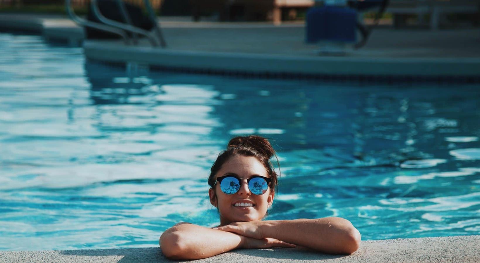 Sparkling swimming pool woman with sunglasses, in a pool, rests her arms on the ledge and smiles